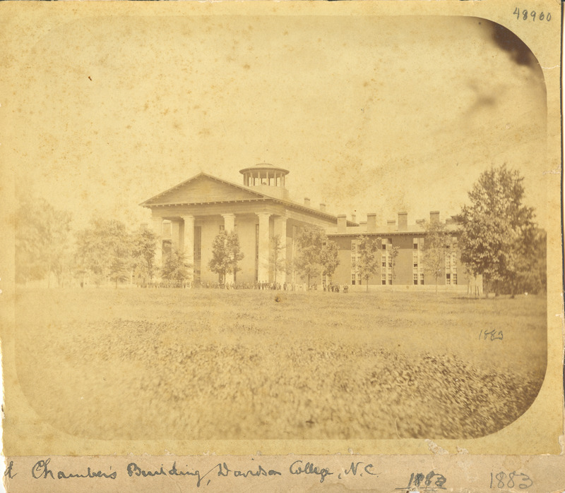 The front of the Old Chambers building shot from a distance with a large group of people gathered in front in 1883
