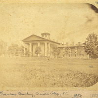 The front of the Old Chambers building shot from a distance with a large group of people gathered in front in 1883