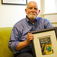 Dr. Randy Nelson in his office, holding a framed copy of Tom Swift in the Caves of Nuclear Fire